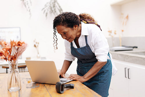 Mature business owner managing online flower orders with a laptop