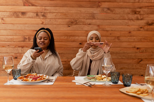 Two female friends taking pictures of their food in a restaurant