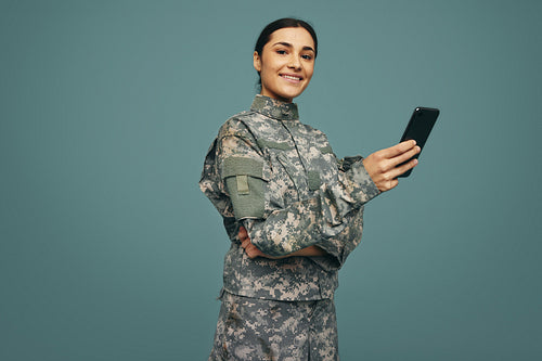 Smiling military servicewoman holding a smartphone in a studio