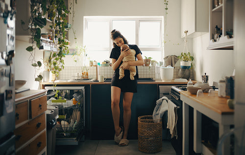 Mother holds baby in bright kitchen at home