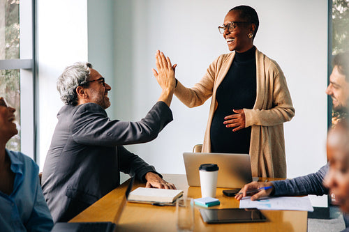 Pregnant woman high-fiving colleague in a casual business meeting