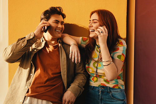 Friends laughing and talking on the phone together against a colorful wall