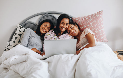 Three girls lying on bed looking at a laptop