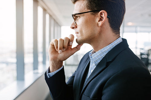 Mature businessman standing by window and thinking