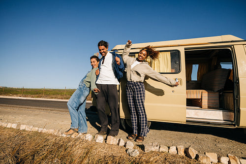 Friends on a road trip pose by a van in sunny open desert landscape
