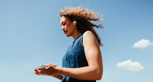 Checking smartphone while listening with earPods under clear blue sky