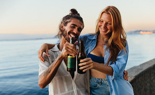 Joyful couple clinking beers at sunset on Urca’s Wall