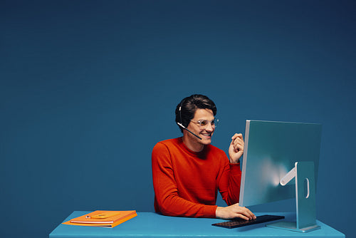 Young man working on computer monitor with headset and eyeglasses
