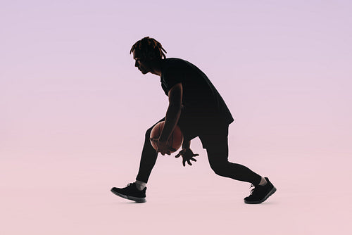 Silhouette of a young basketball player dribbling ball in studio with pink background