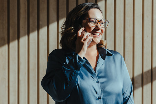 Smiling woman talking on smartphone in sunlit modern office