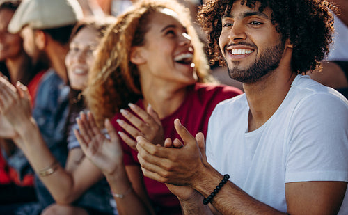 Man clapping while watching a soccer match with friends at stadium