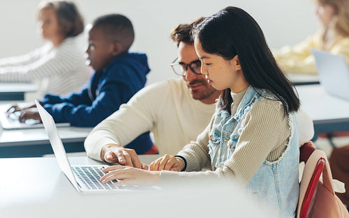 School educator providing assistance to a young student in a coding class