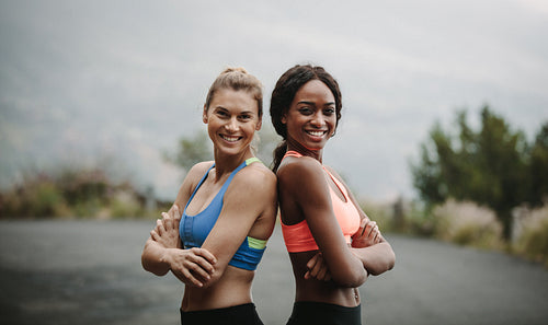 Women in fitness attire on road early in the morning. Fitness women standing with back against each other with folded hands.