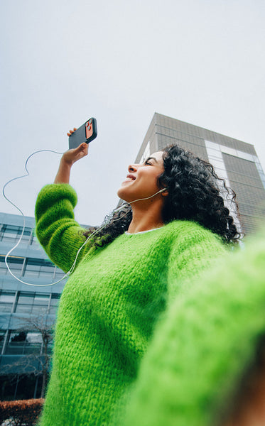 Woman taking selfie outdoors with smartphone and earphones near city building