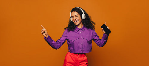 Cheerful woman celebrating with vibrant moves and music on orange background