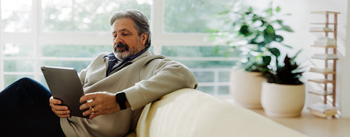 Senior man uses a tablet while sitting at home