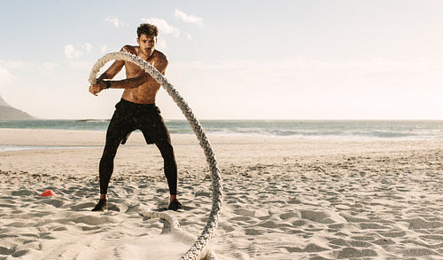 Man doing fitness training at the beach using battling rope