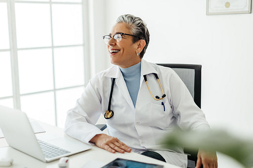 Pensive female doctor sitting in her office, smiling and looking away