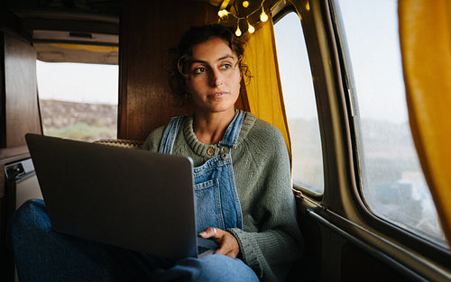 Woman working on a laptop inside a cozy van while traveling
