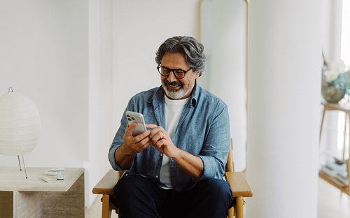 Senior man uses a smartphone while relaxing at home