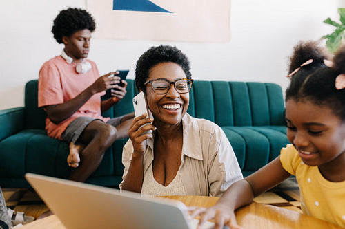 Woman speaking happily on the phone while sitting with her kids in the living room