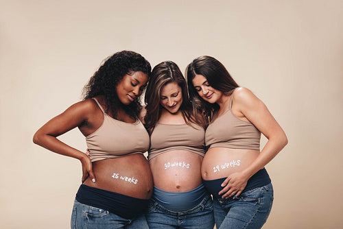 Pregnant mothers smiling at their their baby bumps in a studio