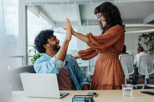 Young business people celebrating success with a high five in an office
