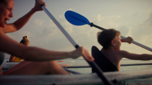 Family enjoys a relaxing clear kayak adventure on calm tropical waters at sunset