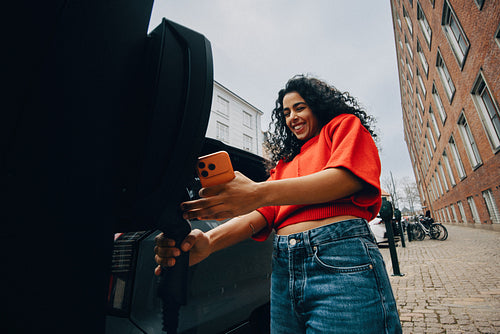 Electric mobility as a woman charges her car on an urban street