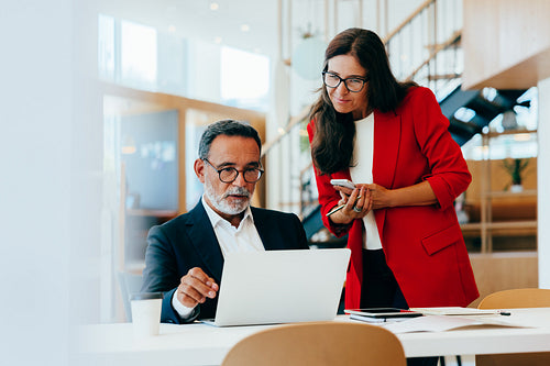 Mature professionals discussing work while viewing a laptop in an open office space