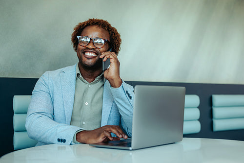Happy businessman on phone call while using laptop at workspace