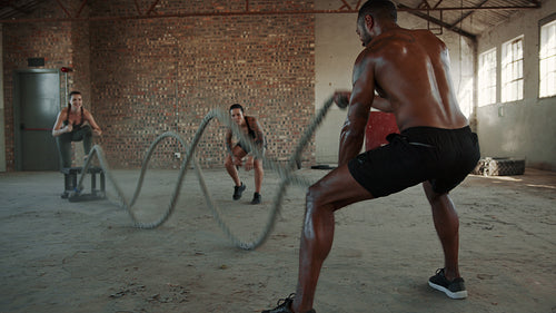 Fitness man doing battle rope workout with instructor