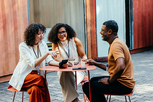Colleagues enjoying a casual outdoor meeting with coffee and smiles