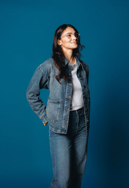 Her denim look frames a woman standing on a blue studio background