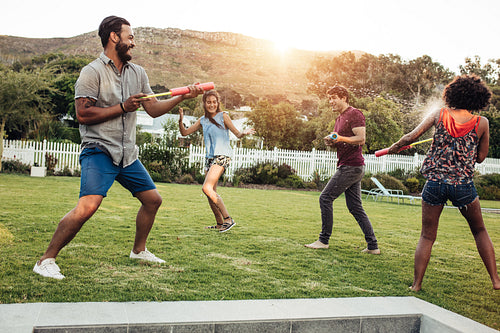 Couple playing with water cylinder tube toys in backyard garden