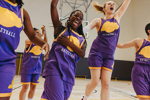 Diverse basketball team celebrating success on indoor court with joy and energy