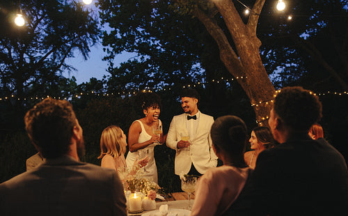 Joyful backyard wedding celebration with couple sharing a toast under string lights
