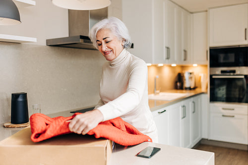 Happy senior woman unpacking her clothing delivery at home
