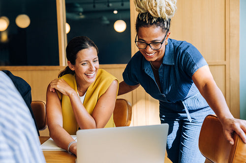 Two professional women smiling and working together at a desk with a laptop