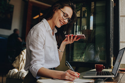 Freelancer at cafe talking on phone and making notes