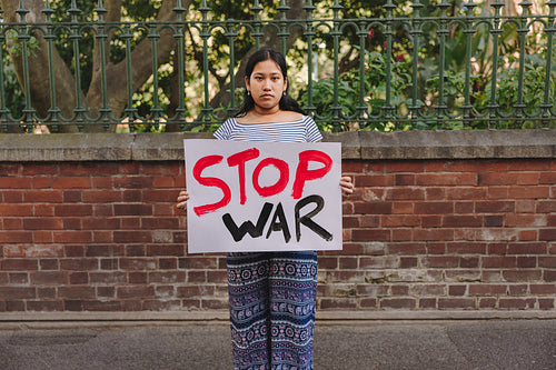 Teenage girl holding an anti-war poster outdoors