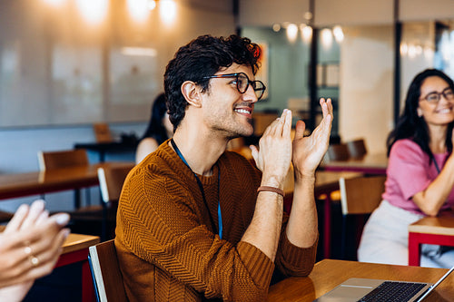 Smiling man claps at laptop in office lounge