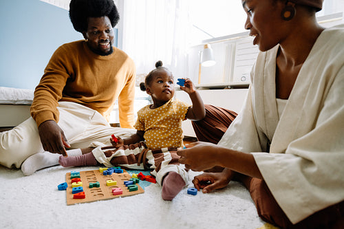 Parents teaching toddler alphabet with colorful blocks at home