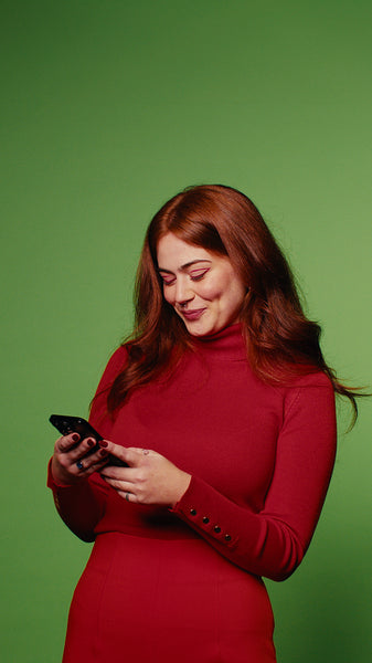 Young woman with red hair smiles at her phone against a green screen background