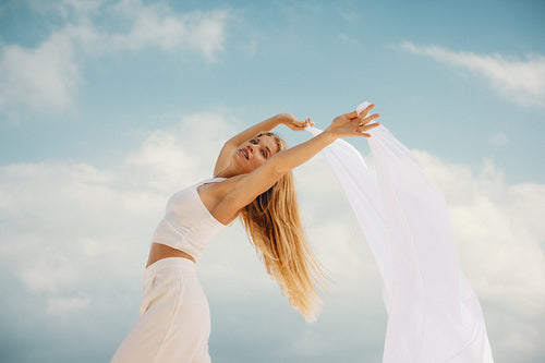 Young woman dancing with airy white fabric in a tranquil outdoor setting