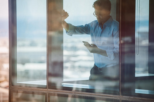 Businessman standing inside office building and using smartphone