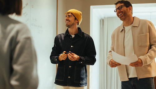 Coworkers discuss ideas at a whiteboard during an office brainst