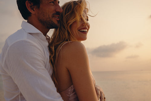 Beautiful couple embracing at sunset on the beach with joyful expressions