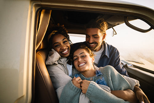 Three friends embracing in a car smiling at the camera