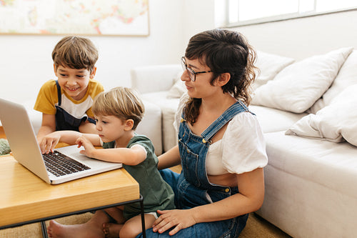 Boy using laptop with his mother and brother looking on